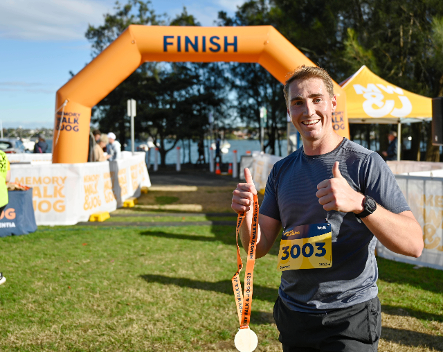 Memory Walk & Jog. Man standing at the finish line with medal.