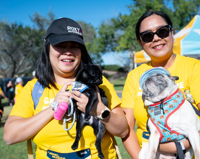 Memory Walk & Jog. Two woman with a dog at the end of the race. Both woman are wearing yellow shirts.